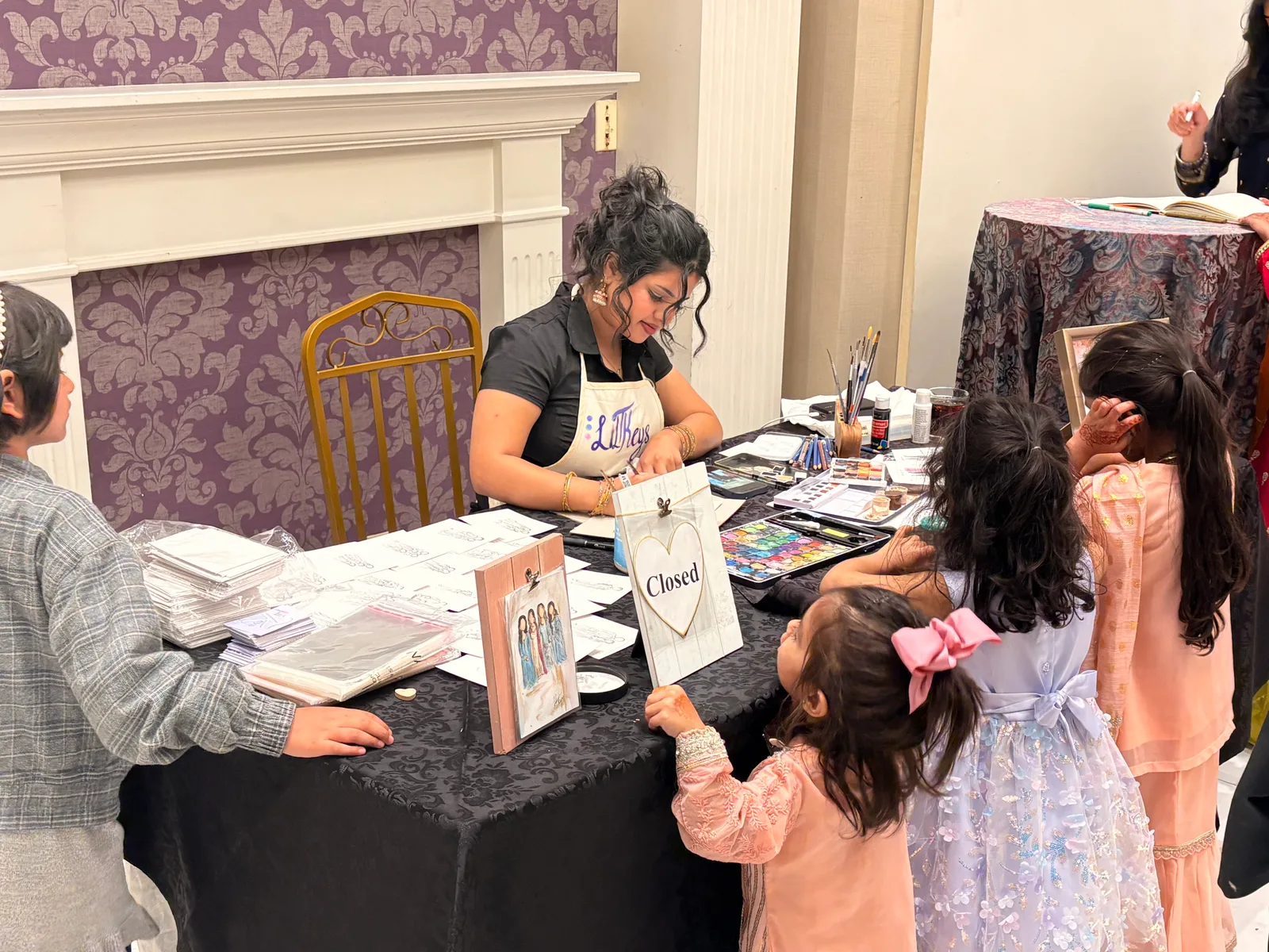 Talia painting live guest illustrations while children watch at an event